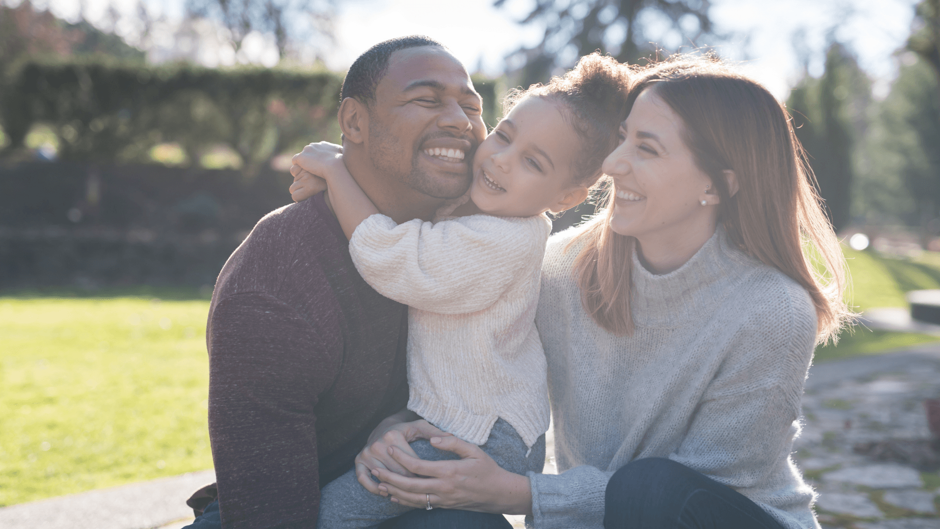 A father, mother, and daughter laughing together outdoors